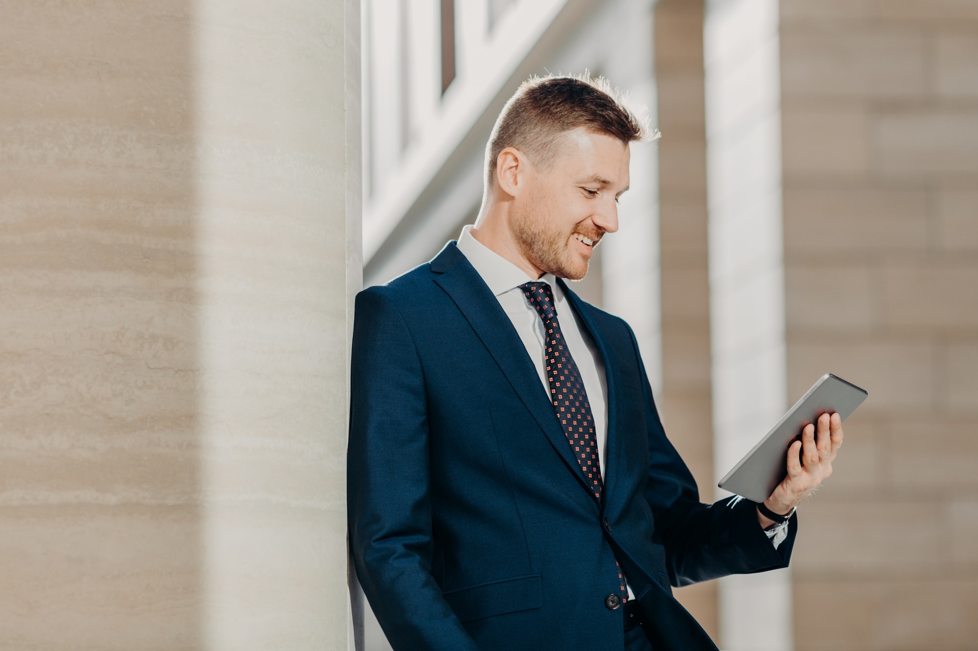 Businessman in formal suit, holds digital tablet in hands and reads SEO Press Releases